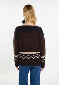 Brązowy sweter dziany o luźnym kroju, z szerokim dekoltem, z geometrycznym wzorem w odcieniach kremowym i ciemnoniebieskim wzdłuż dołu i rękawów.
