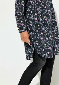 Długa koszula zapinana na guziki w ciemnonawiwowym kolorze, z zabawnym rysunkowym wzorem przedstawiającym twarze i gwiazdy w różowych, żółtych i białych akcentach.