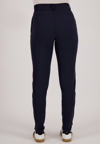 Marineblauwe broek in een slank ontwerp met een taps toelopende pasvorm. Kenmerken zijn onder andere een gladde textuur, achterzakken en subtiele stikseldetails, gecombineerd met witte sneakers.