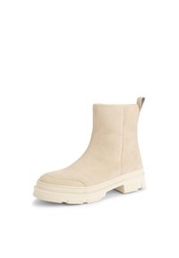 Beige suède enkellaars met een chunky rubberen zool, afgeronde neus en een trekband aan de achterkant, weergegeven schuin naar rechts op een witte achtergrond.