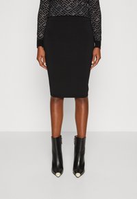 Jupe crayon noire côtelée avec une silhouette ajustée. Associée à des bottines noires chevilles avec des bouts pointus et des accents métalliques.