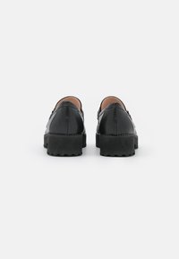 Scarpe in pelle nera con finitura liscia, retro arrotondato e suole spesse e texturizzate. Design minimalista con un leggero tacco.