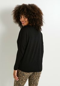 Suéter negro brillante con un corte holgado y mangas largas, combinado con pantalones ajustados de estampado de leopardo. Cuello simple y dobladillo acanalado.