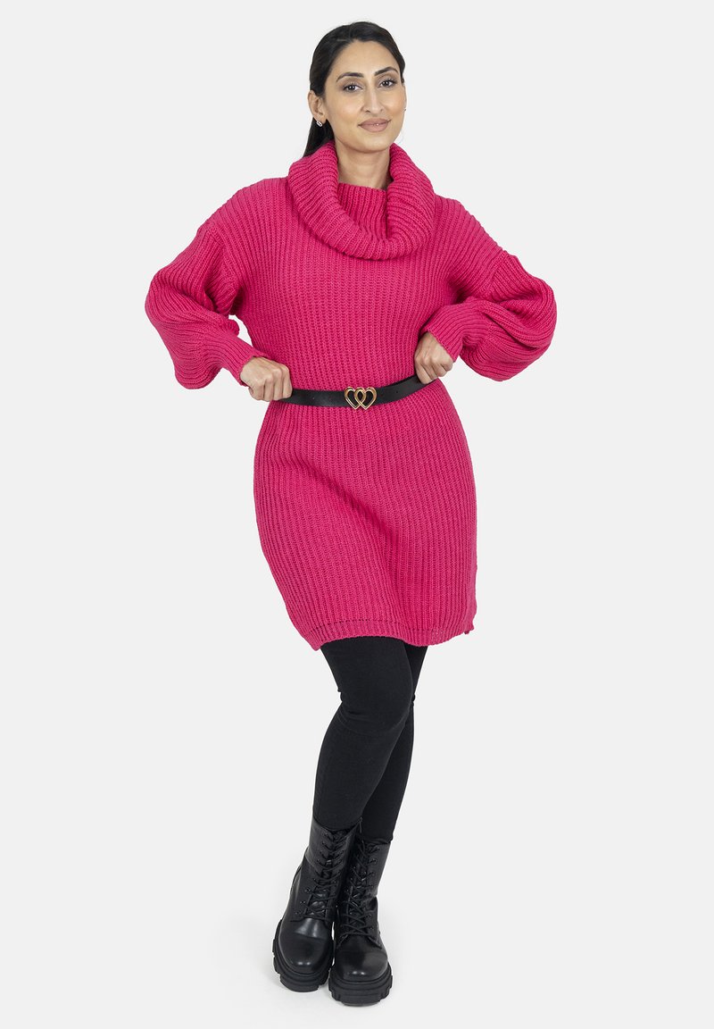 Stort stickat tröja i livlig rosa med en krage, kombinerad med svarta leggings och kraftiga svarta snörstövlar, accentuerad av ett svart bälte.