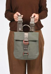 Sac à dos vert avec rabat, bretelles réglables et une boucle rouge bien visible. Fabriqué en matériau durable avec une texture lisse.