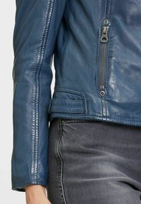 Giacca da motociclista in pelle blu navy con variazioni di trama, zip frontale e tasca, cuciture rinforzate e orlo asimmetrico.