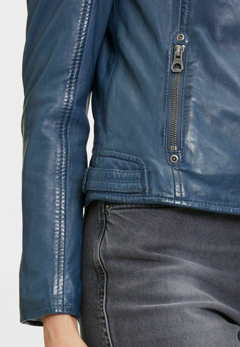 Giacca da motociclista in pelle blu navy con variazioni di trama, zip frontale e tasca, cuciture rinforzate e orlo asimmetrico.