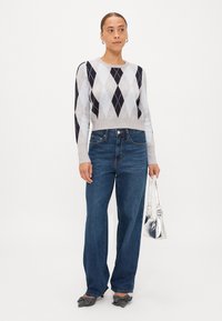 Εφαρμοστό γκρι πουλόβερ με ναυτική διαμαντένια σχέδιο, ψηλόμεσα μπλε τζιν, ασημένια τσάντα και γκρι παπούτσια με φιόγκο.