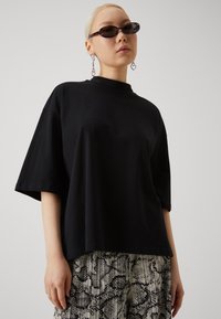 T-shirt noir surdimensionné à manches courtes, avec un col haut. Associé à un pantalon léger à motifs avec un design en imprimé serpent.