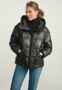 Czarna kurtka puchowa z sztucznej skóry z kapturem, z zamkiem błyskawicznym, bocznymi kieszeniami i pikowanym wzorem. Nosi się ją na czarnym golfie.