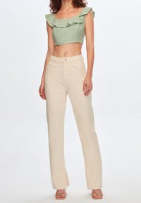Top corto verde con detalles de volantes, combinado con pantalones beiges de pierna recta y cintura alta. Tela suave y tonos naturales.
