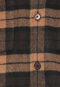 Brown and black plaid flannel shirt featuring two front pockets and a brown button closure. Soft texture with visible stitching.