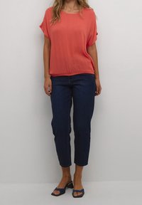 Top corto corallo a maniche corte con una vestibilità ampia, abbinato a jeans in denim blu scuro e sandali navy a fascia con punta quadrata.