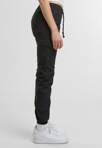 Svart cargobukser med elastisk midje og snor. Har sidelommer og innsnevret design, kombinert med hvite sneakers.