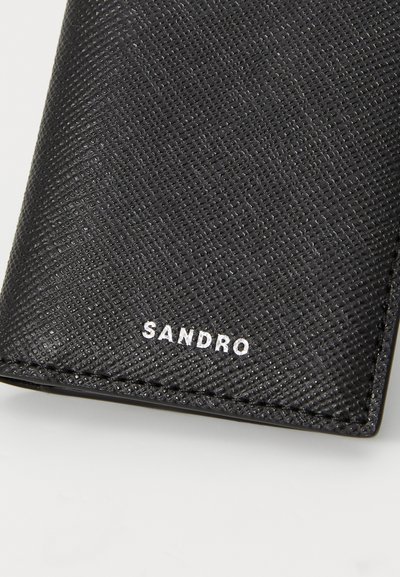 Portofel negru cu textură, având un finisaj neted, ce include un logo alb "SANDRO" și un design structurat. Materialul pare a fi rezistent și sintetic.