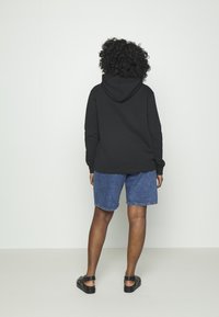 Svart hooded sweatshirt i kombination med blå denimshorts. Tyget verkar mjukt med en avslappnad passform. Sandaler kompletterar outfiten.