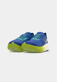 Par de zapatillas de running azules con cordones turquesa y suelas amarillas brillantes, mostradas desde un ángulo frontal bajo sobre un fondo blanco.