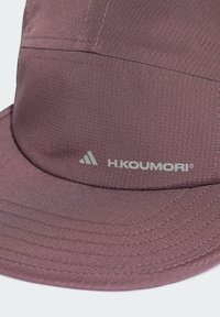 Purple cap made of textured fabric with a stitched design and an embroidered logo on the front. Brim is slightly curved.