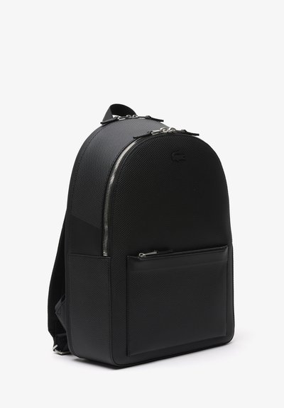 Sac à dos noir avec une finition texturée, un sommet arrondi et des zips argentés, comportant une poche avant et un accent logo sur la partie supérieure.