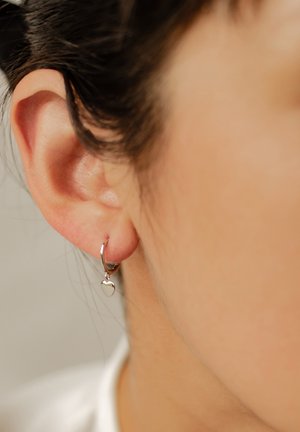 Silberne Creolen mit einem kleinen, herzförmigen Anhänger. Das Design ist schlank mit einer polierten Oberfläche und zeigt einen minimalistischen Stil.