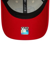 Red baseball cap with a black visor, featuring a holographic NFL logo sticker on the brim and a mesh inner lining.