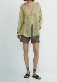Lichtgele, polyester lange mouw overhemd met knopen en een V-hals en een textuurpatroon, gecombineerd met bruine shorts en zwarte sandalen met bandjes.