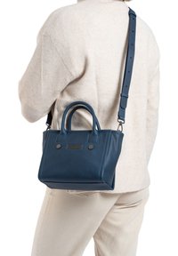 Sac à main en cuir bleu avec de courtes poignées et une longue bandoulière réglable. Présente des accents en métal noir et un détail texturé horizontal à l'avant.