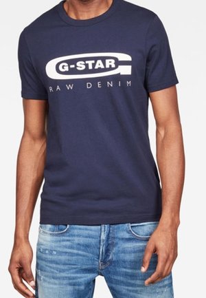 Granatowa bawełniana koszulka z wyraźnym białym logo, które brzmi "G-STAR RAW DENIM" na klatce piersiowej. Krótkie rękawy i okrągły dekolt.