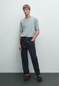 Light green cotton crew-neck t-shirt, relaxed fit, paired with dark denim straight-leg pants and brown suede shoes. Simple, modern design.
