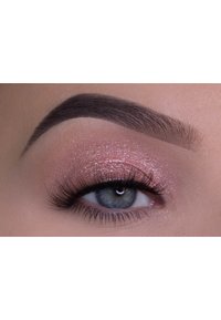 Primo piano di un occhio con ombretto rosa scintillante, sopracciglio scuro e definito, lunghe ciglia e iris blu-verde su uno sfondo neutro.