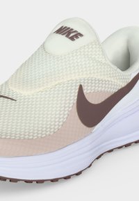 Λευκό και μπεζ παπούτσι τρεξίματος Nike με καφέ λογότυπο Swoosh και επάνω μέρος από διχτυωτό υλικό, με χοντρή λευκή σόλα και επενδεδυμένο κολάρο.