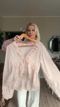 Blusa rosa cipria a maniche lunghe con rifiniture in pizzo arricciato, dettaglio con fiocco al collo e maniche arricciate. Tessuto leggero e strutturato.