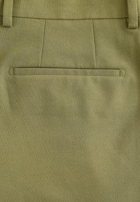 Olijfgroene broek met een gladde textuur; heeft een enkele achterzak en een taillerend ontwerp; de stiksel lijkt netjes en geïntegreerd te zijn.