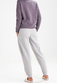 Pantalones de chándal gris claro con bolsillos laterales y puños elásticos, combinados con una sudadera morada oscura con dobladillo y cuello acanalados.