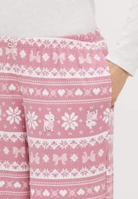 Rozā rakstainas pidžamas bikses ar baltām sniegpārsliņām, sirdīm un lentītēm, rotātas ar dekoratīvu jostasvietu un sānu kabatām. Mīksts, fakturēts audums.