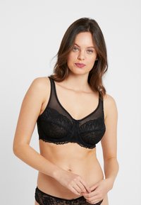 Black lace bra featuring sheer panels, floral patterns, scalloped edges, adjustable straps, and a small bow detail at the center front.