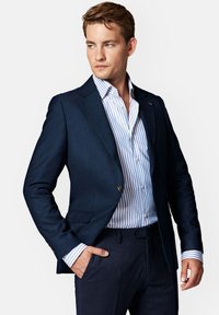 Granatowa marynarka o dopasowanym kroju, teksturowany materiał, z jednolitym zapięciem na guzik, w połączeniu z białą i niebieską w paski koszulą oraz dopasowanymi ciemnymi spodniami.