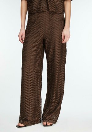 Brązowe spodnie o szerokich nogawkach z wzorem z koronką w jodełkę, noszone z dopasowanym topem i czarnymi sandałami na kwadratowym nosku.