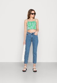 Top com padrão zebra em verde e branco, jeans de cintura alta azuis com pontos azul claros, sandálias brancas e uma bolsa de ombro branca.