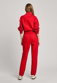 Camisa y pantalones de mezclilla rojos, con un corte relajado, detalles de botones y mangas remangadas. Textura suave con un color uniforme.