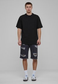 Camiseta negra de gran tamaño con mangas cortas, combinada con pantalones cortos de mezclilla oscura con dobladillos deshilachados y múltiples detalles rasgados. Calcetines blancos y zapatillas.