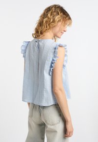 Top senza maniche di un blu chiaro con spalle arricciate, tessuto testurizzato e dettaglio alla schiena con apertura a chiave. Design informale, vestibilità rilassata.