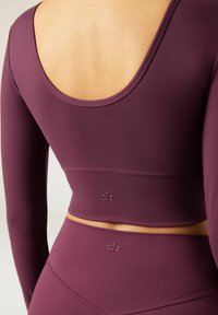 Bordeauxfarbener, taillierter Langarm-Crop-Top mit einem runden Rückenausschnitt, ausgestattet mit einem strukturierten Stoff und einem dezenten Markenlogo nahe dem Saum.