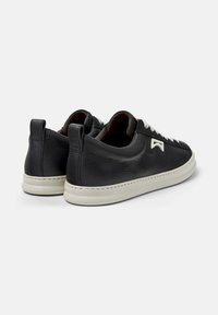 Pair of black low-top leather sneakers with white soles and laces, featuring a small white logo on the side, shown from the back angle.