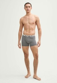 Fekete és fehér szívmintás boxer alsónadrág, fehér derékrésszel, amelyen a "TOM TAILOR" logó található. Puha anyag és testhezálló kialakítás.