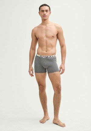 Boxershorts im schwarz-weißen Herzmuster, mit einem weißen Bund, auf dem das Logo "TOM TAILOR" steht. Aus weichem Stoff und mit engem Schnitt.