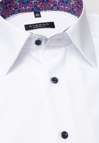 Camisa blanca de vestir con botones azules. Presenta un tejido estampado en el interior del collar con un diseño floral en azul, rojo y púrpura. Etiqueta de corte cómodo.
