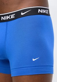 Κοντινή λήψη μπλε εσώρουχα τύπου μποξεράκια Nike που φοριούνται από άτομο, με μαύρη ζώνη μέσης με λευκό λογότυπο Nike και μικρό λευκό σήμα στην αριστερή μηρό.