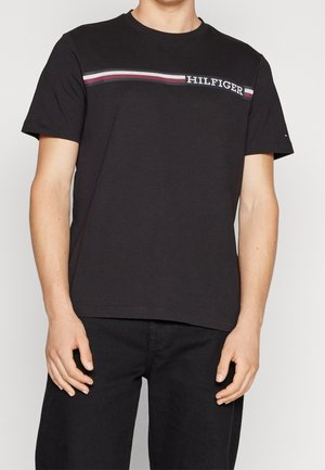 Homme portant un T-shirt noir à manches courtes avec des rayures horizontales blanches, rouges et bleues et le texte « HILFIGER » sur la poitrine.