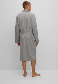 Accappatoio grigio in cotone con colletto alla sciarpa, maniche lunghe, cintura in vita, tasche laterali e una vestibilità comoda, che arriva a metà polpaccio.